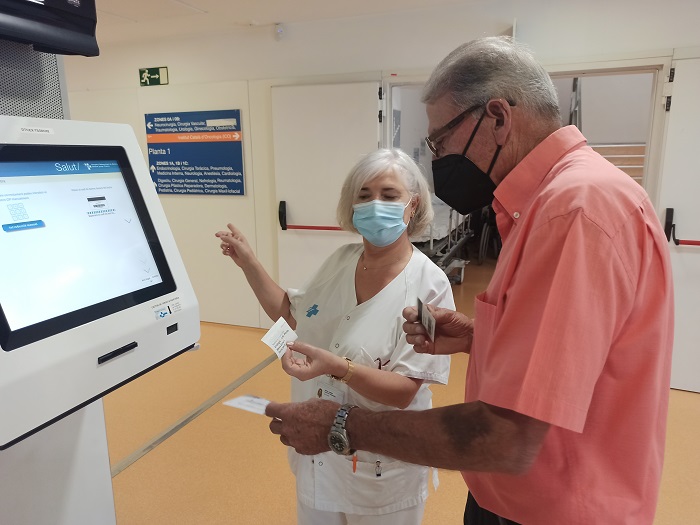 Un pacient traient el seu tiquet d'arribada, amb una treballadora explicant el nou sistema d'avís