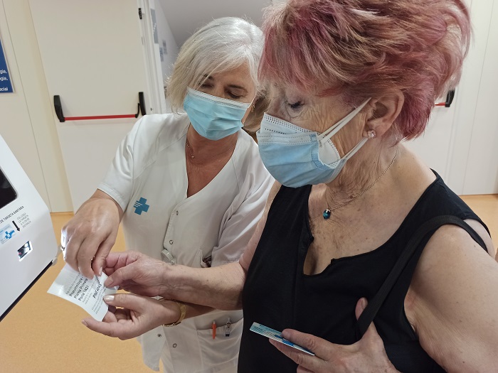 Una pacient traient el seu tiquet d'arribada, amb una treballadora explicant el nou sistema d'avís