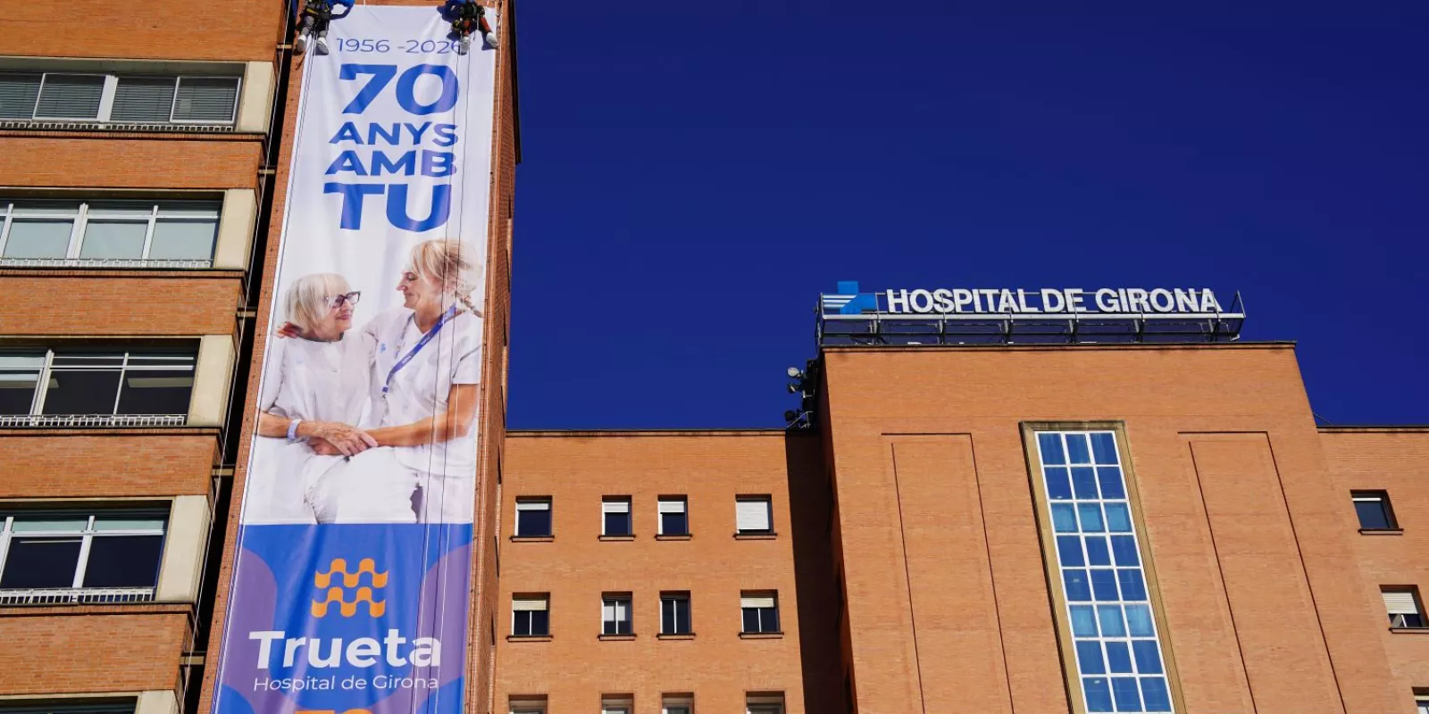 Operaris instal·len a la façana de l'Hospital Trueta la lona commemorativa del 70è aniversari del centre