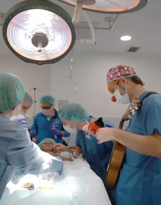 Un infant al quirofan durant la inducció anestèsica acompanyat per un familiar i un representant de Pallapupas