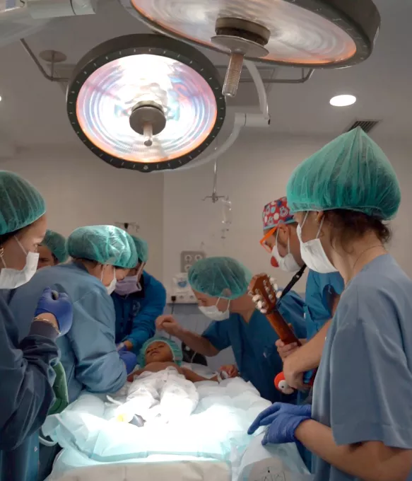 Un infant al quirofan durant la inducció anestèsica acompanyat per un familiar i un representant de Pallapupas