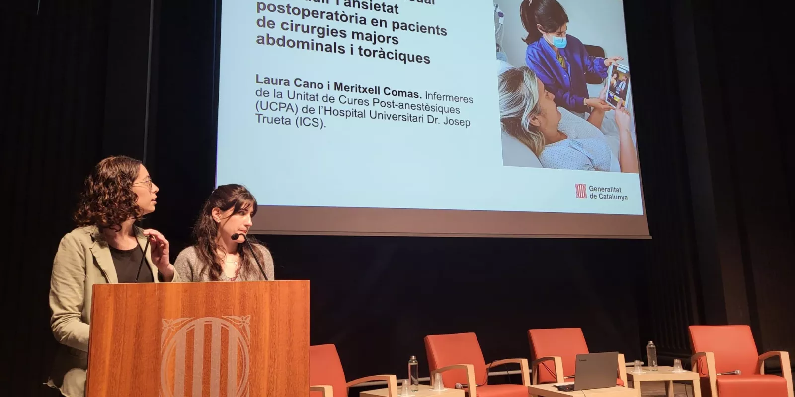 Les infermeres Laura Cano i Meritxell Comas exposen el seu estudi sobre la reducció de l'ansietat postoperatòria mitjançant distracció audiovisual i musical durant la jornada d'experiència del pacient.
