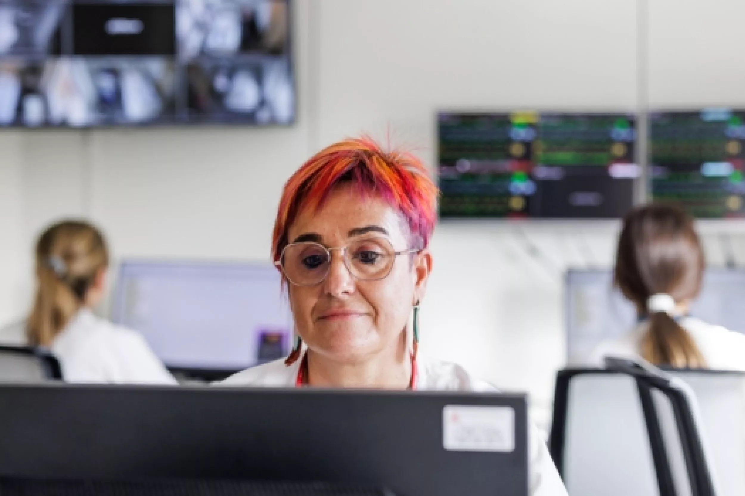 Una trabajadora utilizando el ordenador, y en el fondo aparecen dos trabajadoras con sus ordenadores