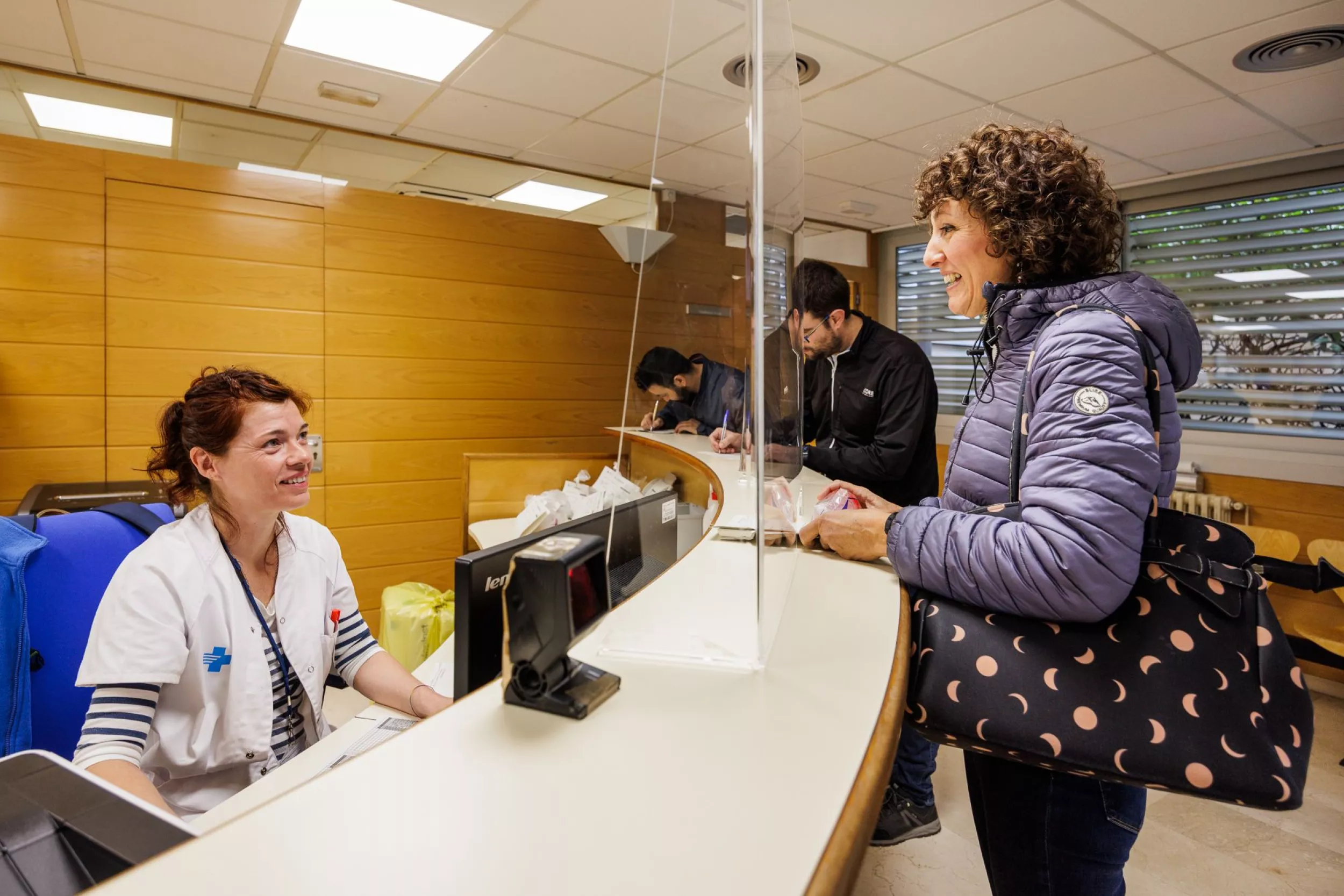 Administrativa d'atenció primària oferint assistència a una dona al taulell d'un centre