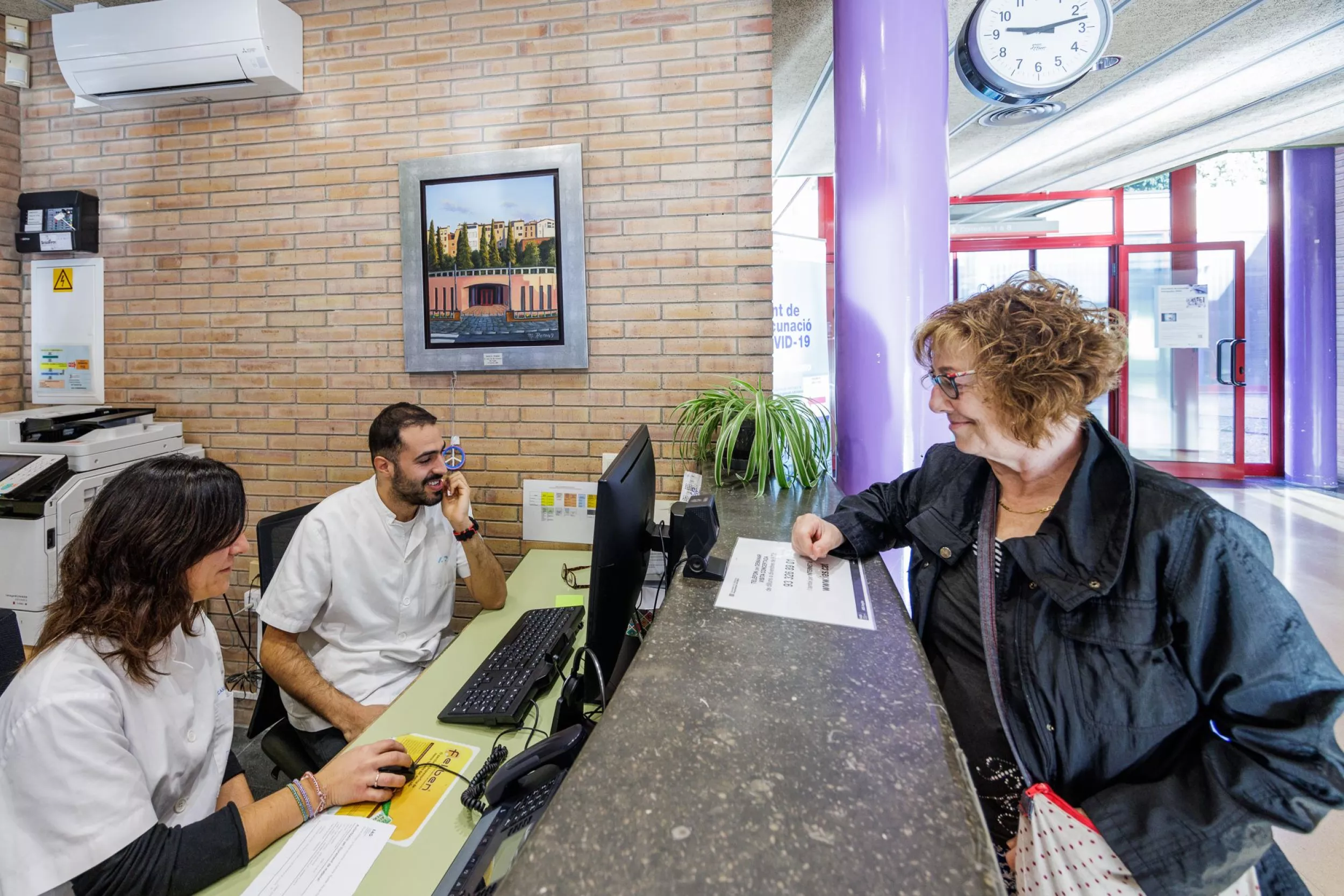 Mostrador de administración del CAP con una trabajadora hablando con una paciente