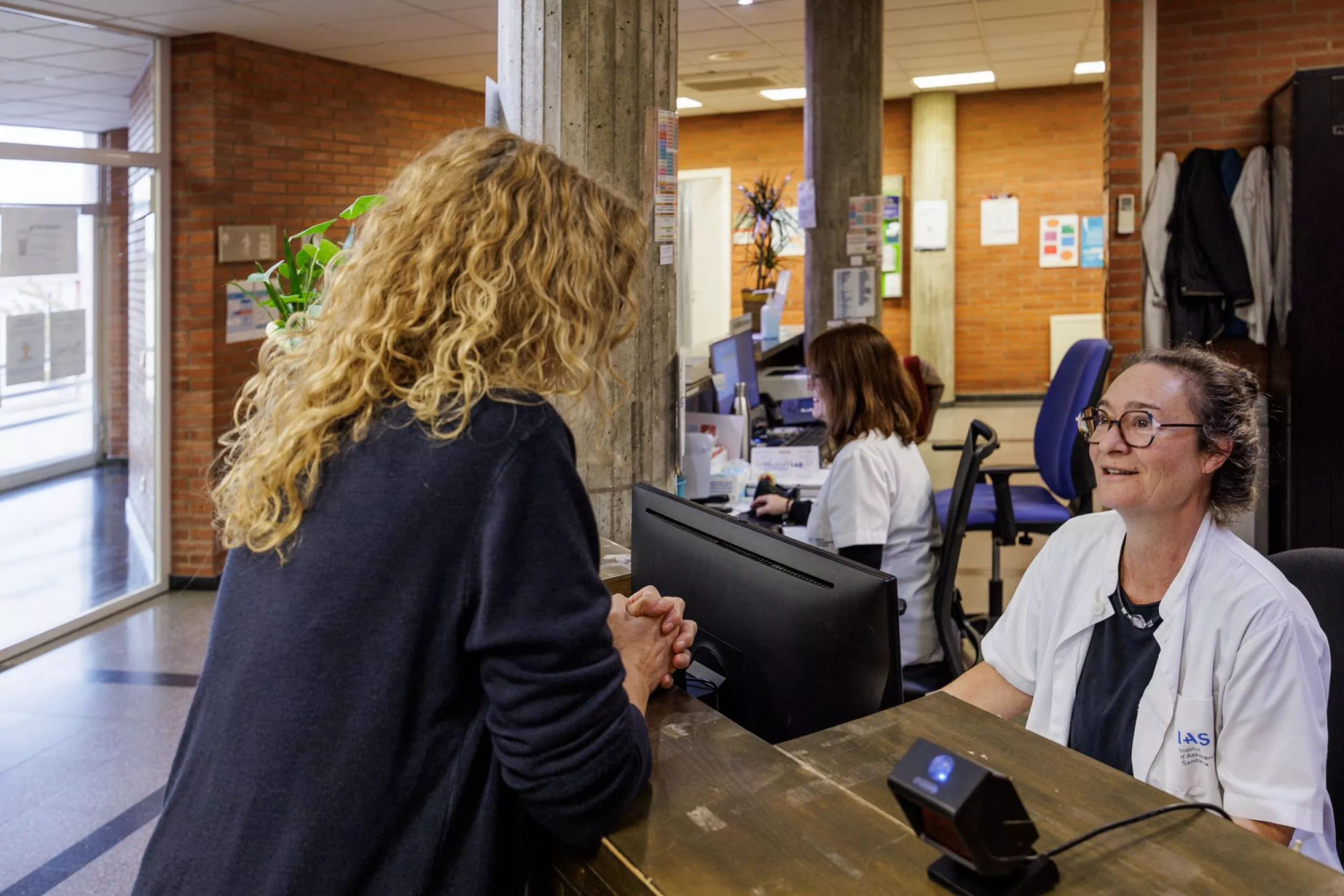  Taulell d'administració del CAP amb una treballadora parlant amb una pacient
