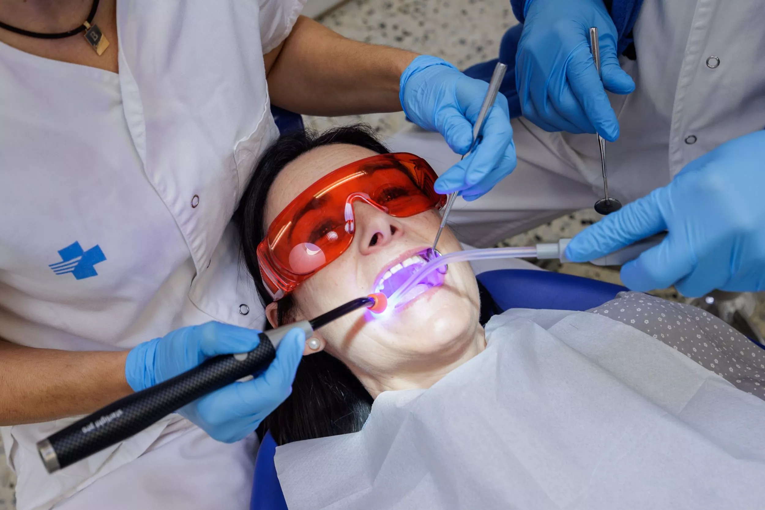 Pacient en una revisió odontològica amb professionals de la salut, llum de polimerització i ulleres de protecció