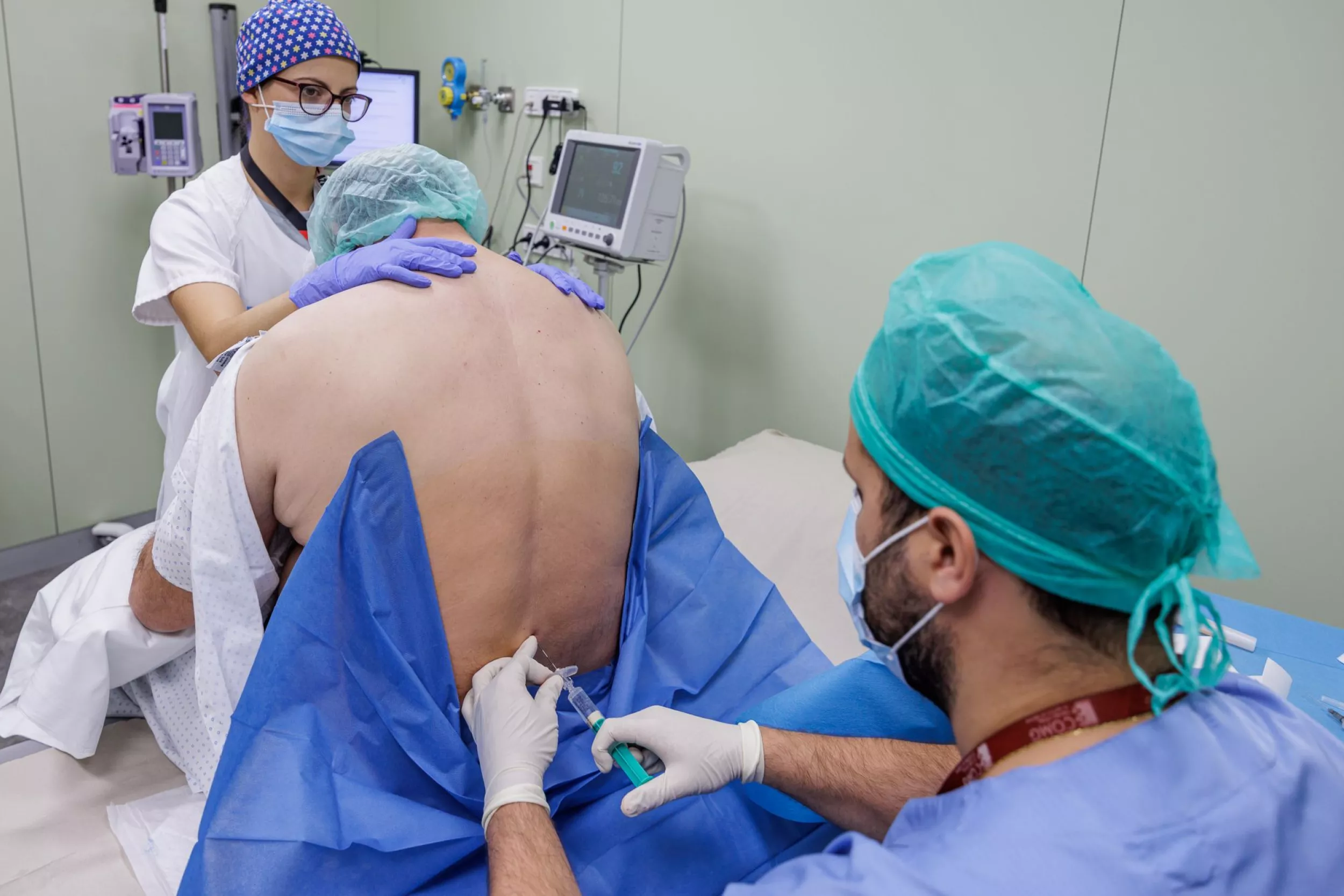 Metge posant anestèsia a l'esquena a un pacient. La infermera subjecta al pacient