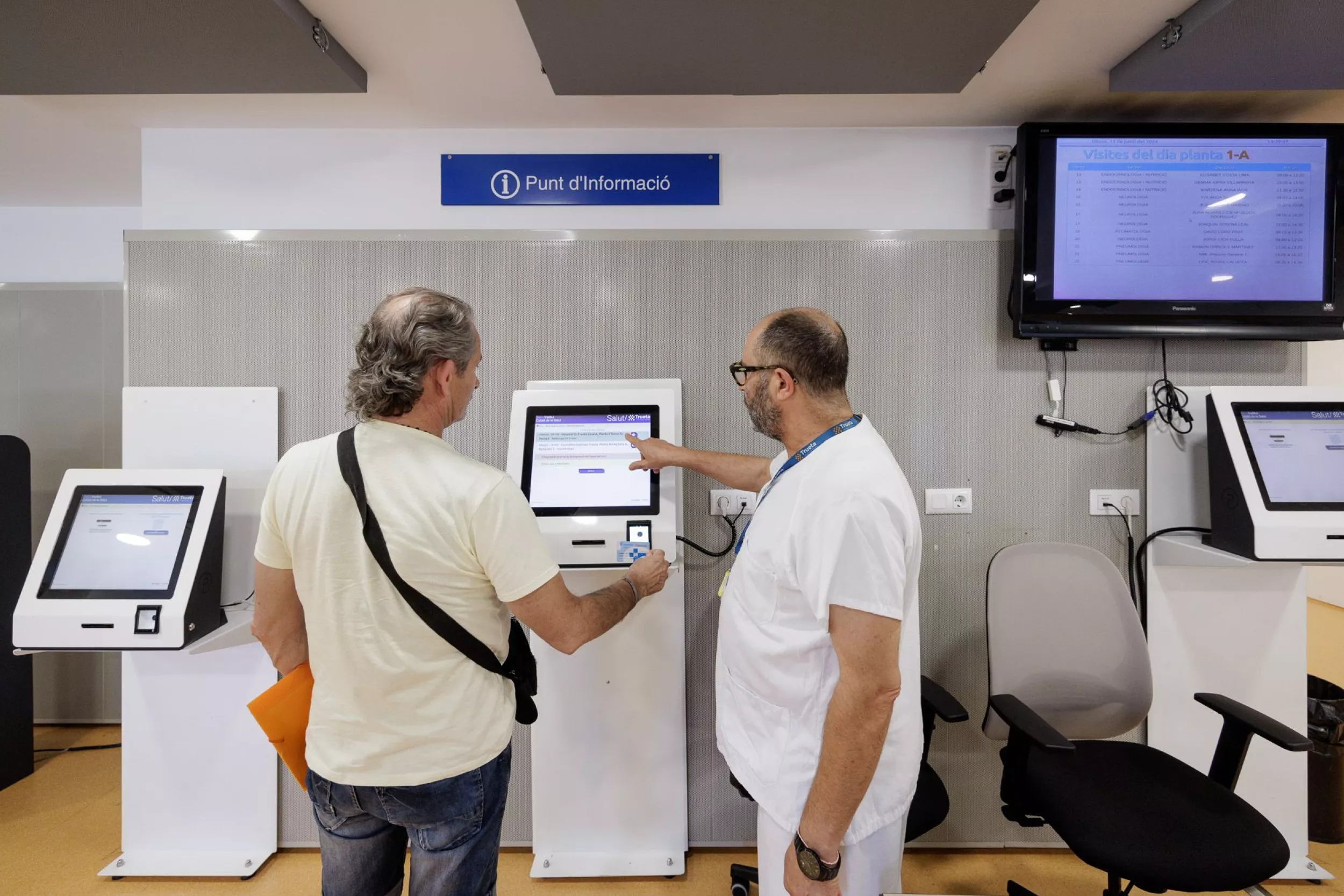 Un professional sanitari ajuda un usuari a utilitzar una màquina d’autoservei al punt d’informació d’un centre de salut