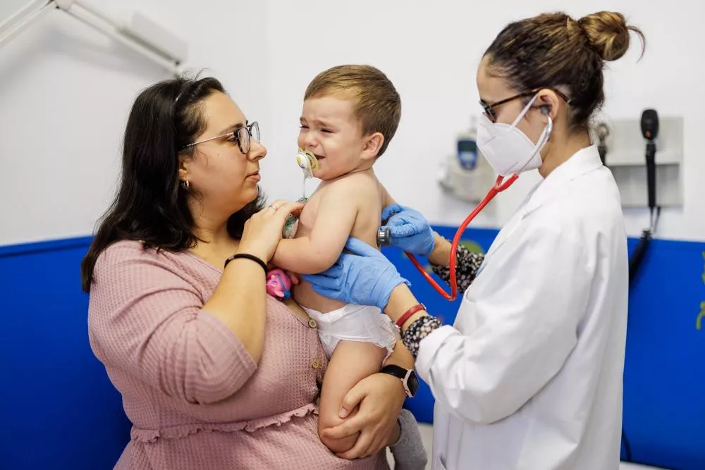 Madre sosteniendo a su bebe mientras un médico ausculta la espalda del bebe