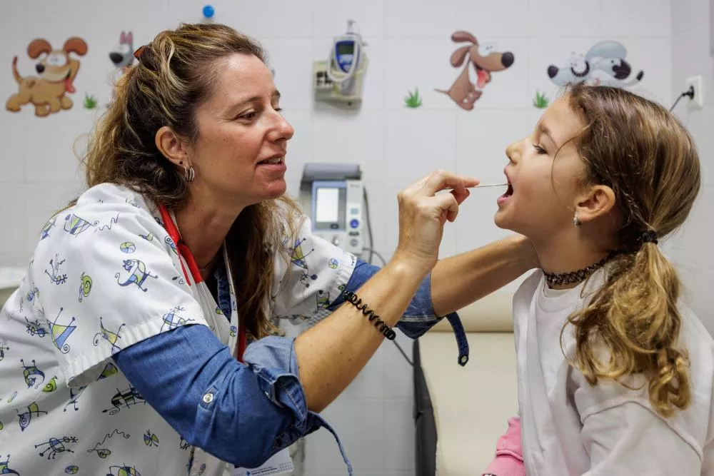 Médico con una niña metiéndole un bastoncillo en la boca