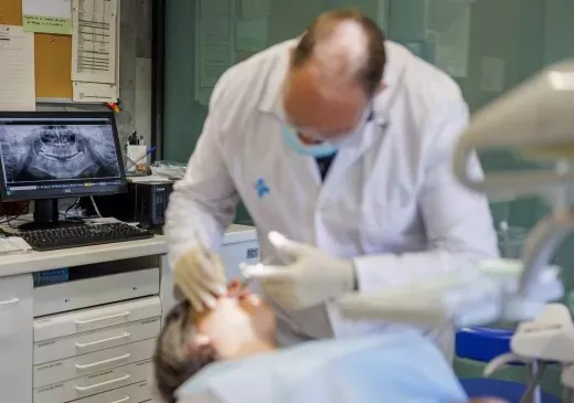 Un dentista atendiendo una paciente, con un monitor con la radiografía de la boca detrás.
